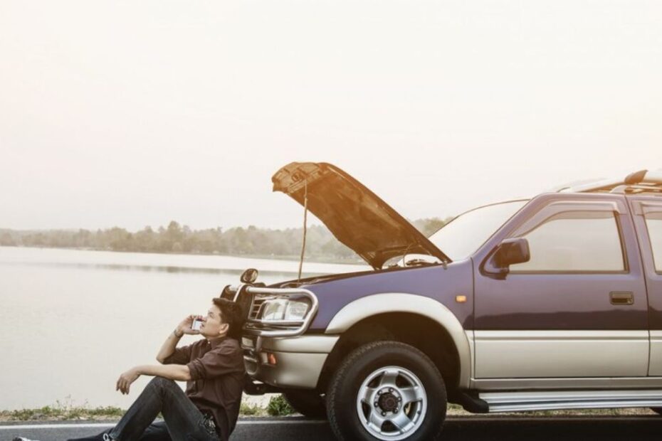 Homem encostado em seu carro quebrado.