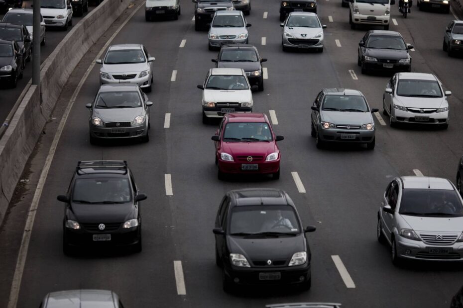 Trânsito de carros com cores neutras e um carro vermelho no meio deles.