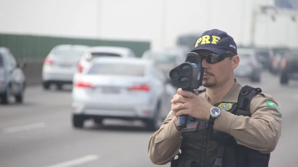 Policia de frente apontando o radar portátil para os carros.