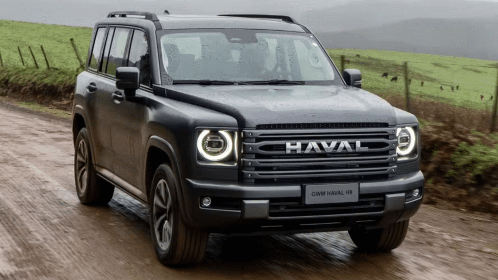 GWM Haval H9 2026 cinza de frente com os faróis acesos em uma estrada cheia de lama.