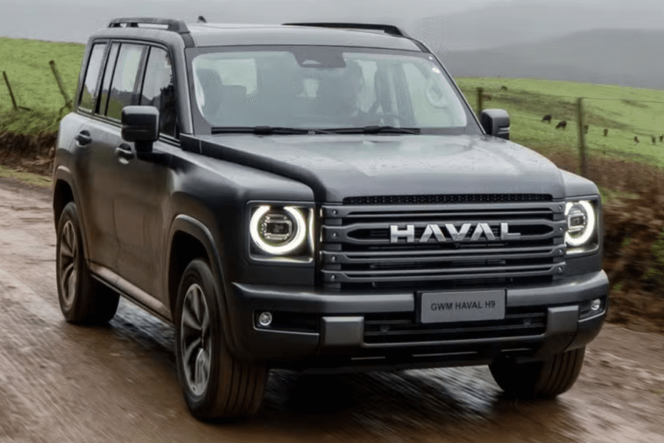 GWM Haval H9 2026 cinza de frente com os faróis acesos em uma estrada cheia de lama.