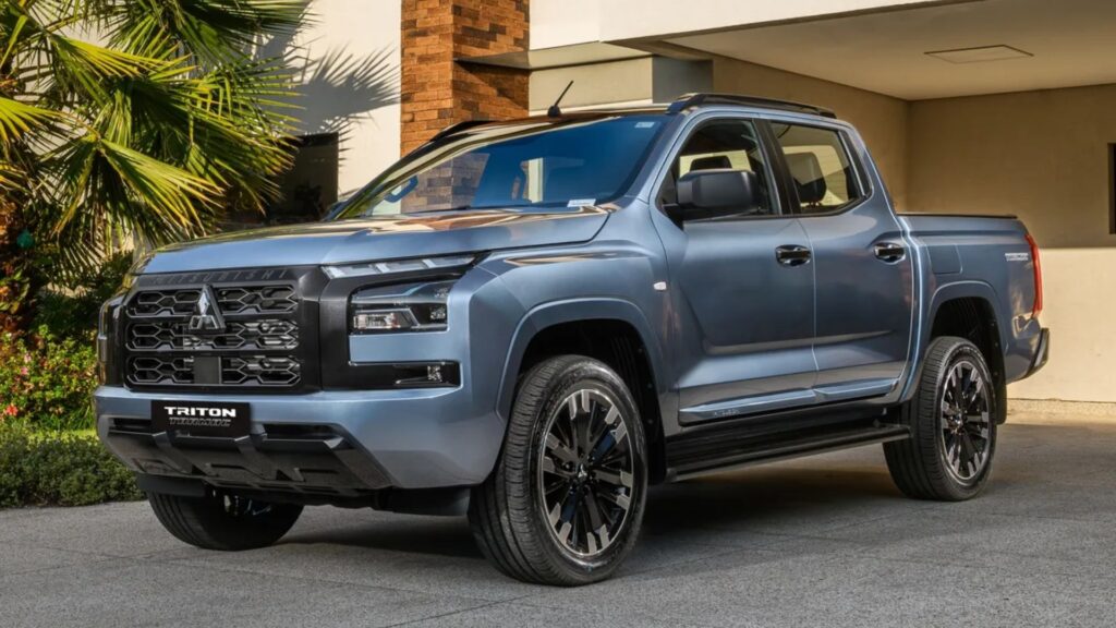 Mitsubishi Triton Tarmac azul parado na diagonal na frente de uma garagem.