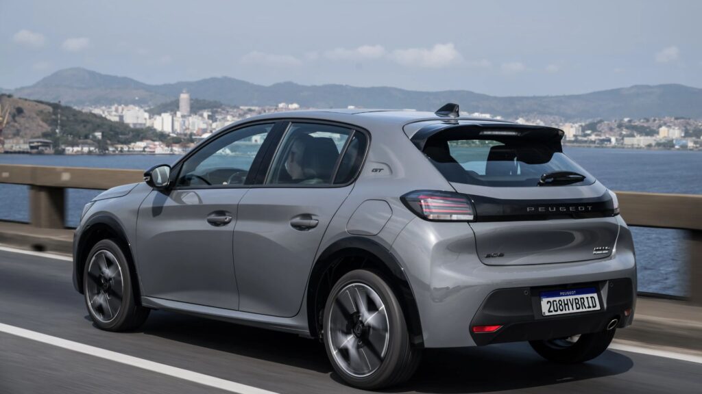 Peugeot 208 2026 cinza acelerando na estrada com um mar do lado.